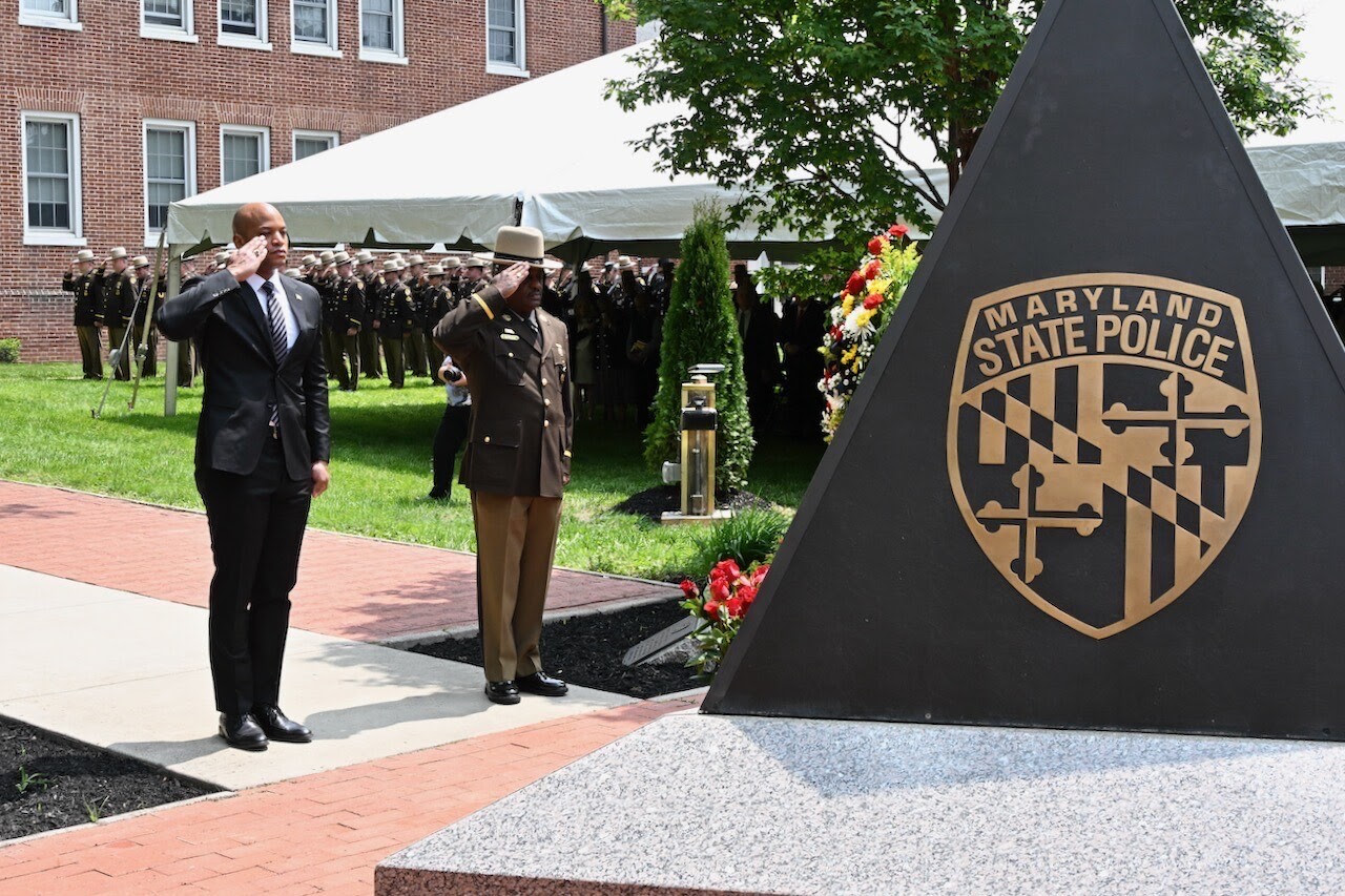Governor Moore and Maryland State Police officer saluting memorial